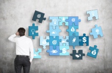 An image of a confused man standing in front of a large blue puzzle with missing pieces against a grey wall